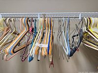 Group of assorted plastic, metal and wood hangers on rail