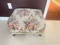 Top perspective of floral tapestry ottoman showing overall fabric pattern and wooden legs