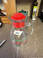 Front view of glass pitcher showing cherry motif and red lid