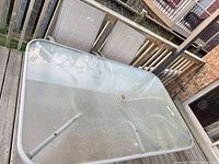 Top view of rectangular glass patio table with umbrella hole, metal frame, folding legs; two sling chairs leaning against railing