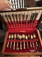 Open wood case showing dinner knives in lid slots, forks, spoons arranged in base