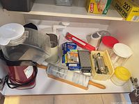 Cupboard view showing marble rolling pin, grater, electric appliances, plastic containers, cookie press parts, Reynolds boxes