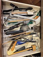 Drawer view of assorted utensils showing metal tongs, turners, spatulas, wooden spoons, ladle and small tools
