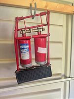 Front view of red double-cylinder foot pump hanging, shows pedal pad and overall design