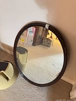 Front view of round mirror leaning against wall, shows dark brown wood frame and reflective glass