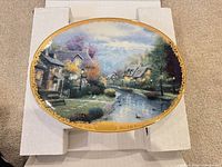 Front view of oval decorative plate showing village scene and gold trim