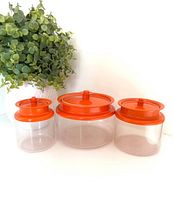 Three clear canisters with orange lids displayed in size order