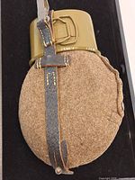 Front view of canteen in wool cover with leather strap and attached metal cup