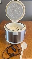 Rice cooker with lid open showing steaming tray, spoon and power cord