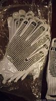 Stack of white cotton knit gloves showing black PVC dot grip pattern on palms inside plastic bag