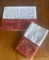 Two hand towels folded showing white terry and red/gold poinsettia satin band
