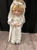 Full view of porcelain bride doll in white dress and veil standing on wood floor