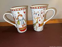 Front view of both 222 Fifth holiday latte mugs showing penguin and reindeer designs