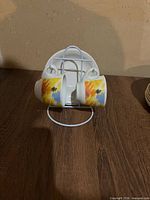 Front view of two cups with abstract pattern hanging on rack, saucers behind