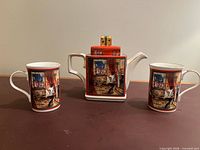 Front view of teapot with lid between two matching mugs