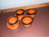 four ceramic terracotta pots with two saucers on surface