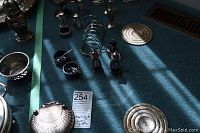 Assorted silverplate and sterling serving pieces arranged on carpet including goblets, candlesticks, salt and pepper shakers, toast rack, small bowls and spoons, trays, and jars.