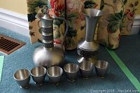 Full set with two pewter pitchers and six matching cups arranged on carpet.