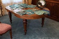 Front and side view of the antique walnut dining table in a carpeted room with a set of cutlery on its surface.