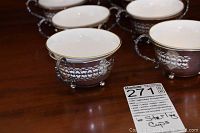 Five china teacups placed inside sterling silver double-handled holders on a wooden table with a tag indicating lot number.