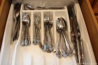 Drawer with adjustable white plastic tray containing neatly arranged flatware: forks, spoons, knives with floral detailed handles
