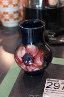 Front angled photo showing the bulbous vase with dark blue background and large pink flower with detailed center and leaves.