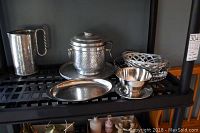 Photo showing a hammered water pitcher with handle, an ice bucket with lid and side handles on a round tray, a small oval hammered platter, a small footed bowl stamped Broms Sweden, a small smooth bowl (Oneida), and two round decorative metal lattice baskets.