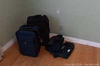Two soft shell suitcases, one dark blue and one black, standing upright on wood floor against wall