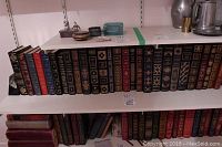 Second-from-bottom shelf showing approximately ten gilt-stamped leatherette bound books and small decorative items