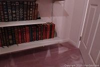 White shelving unit holding leather-bound books on two shelves with a granite bookend on right side of bottom shelf