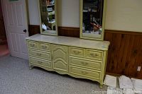 Yellow painted wood dresser with 6 drawers and central cupboard door, decorative handles, ornate legs, two matching framed mirrors above.