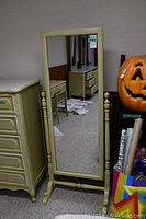Frontal view of the chevalier style mirror, showing the full rectangular mirror and side posts, next to a dresser and a large pumpkin decoration.
