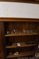 Shelf with assorted clear glass animal figurines, yellow glass penguin, dark ceramic snake, and small stone and ceramic animal figurines.