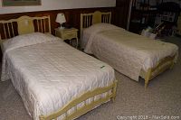 Two twin beds with yellow painted wooden frames, beige quilted bedding, and rails visible under the bedding.