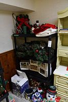 View of black shelving unit holding multiple items of holiday decor including wreaths, gift boxes, figurines, stockings, and mugs.