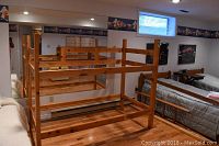 Pine wood twin bunk bed frame in a basement room with wooden floors, showing the frame from front and side angles without mattresses.