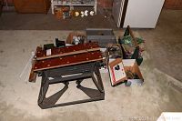 Black & Decker collapsible workbench folded with assorted tools and hardware boxes around it on carpeted floor.