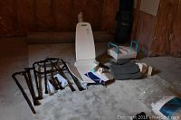 Neptune reclining bath lift, assistive walkers and canes, ObusForm seat cushion, and plastic toilet seat with arm supports laid out on carpeted floor.