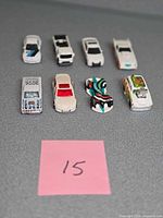 Eight toy vehicles arranged in two rows on grey surface with pink label 15