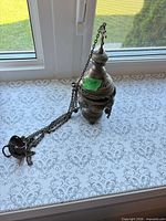 Full view of metal censer with chains displayed on windowsill