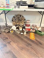 Entire lot arrangement showing wreath, glassware, candle holders, tins, barometer, linens and tissue cover