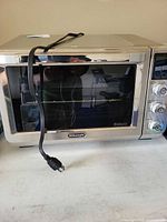 Front view of DeLonghi stainless steel toaster oven showing glass door, rack, power cord