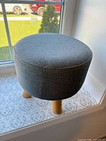 Full view of round grey fabric foot stool on window sill