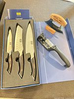Knife set box open showing three Hoshanho knives and additional sharpener and ulu on surface