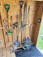 Group of assorted long-handled tools hanging in shed