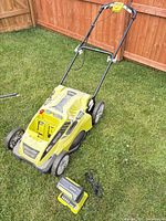 Full view of Ryobi lawn mower with battery and charger on lawn