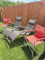 Two zero-gravity recliners and two red camp chairs set on lawn