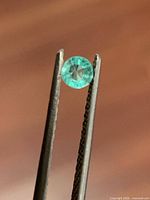 Round green emerald held in tweezers close-up
