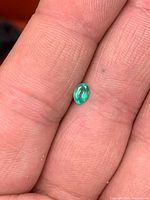 oval green emerald on fingertip, showing size and cut