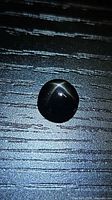 Round black cabochon gemstone on textured surface, star effect visible